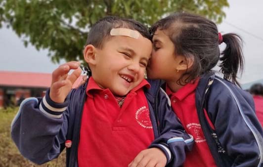 Young school girl kissing a laughing boy's cheek who has a plaster on his forehead - Challenges Abroad