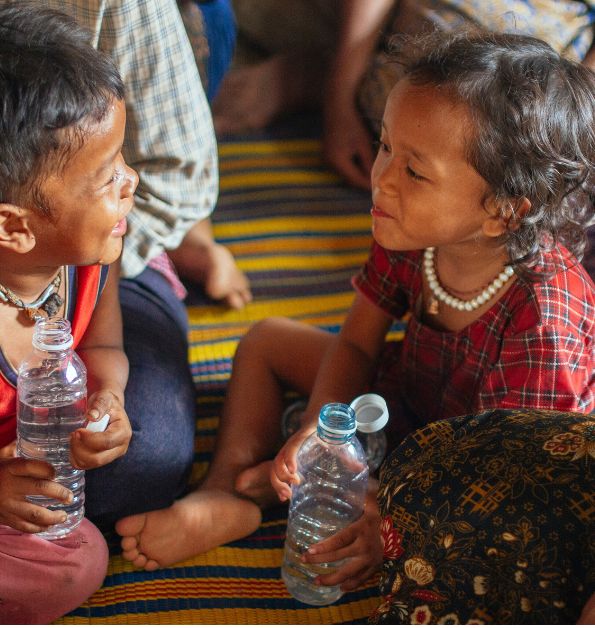 Two children smiling at each other while holding bottles of water - Challenges Abroad