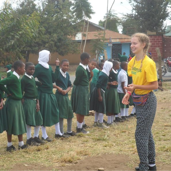 Challenges Abroad team member stood infront of a group of children in school uniform for the sports challenge in Tanzania