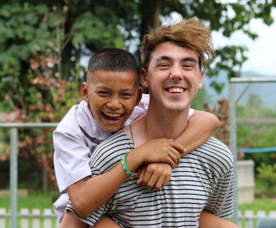 Laughing child being given a piggy back by volunteer - Challenges Abroad