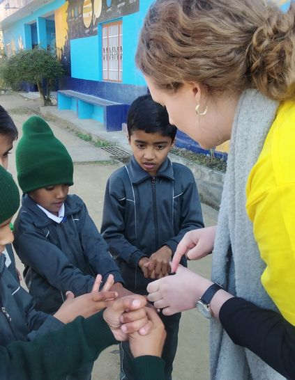 Children in a circle with a challenges abroad member clasping their hands together.