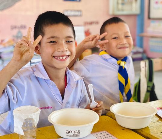 Two kids holding up peace sign fingers while sat infront of bowls- Challenges Abroad